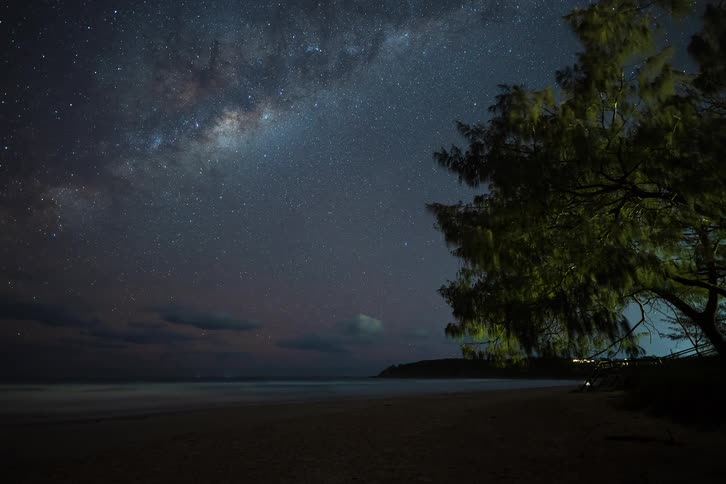 A breathtaking timelapse shows the Milky Way galaxy and countless stars moving across the night sky above a tranquil beach with a lone tree