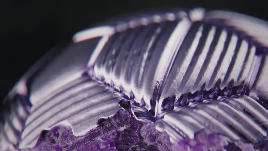 A purple liquid morphs and solidifies into a soccer ball, forming an intricate, ribbed, and textured metallic surface