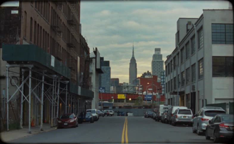 An old film-style shot of a New York City street with the Empire State Building in the distance ends with a dramatic light leak