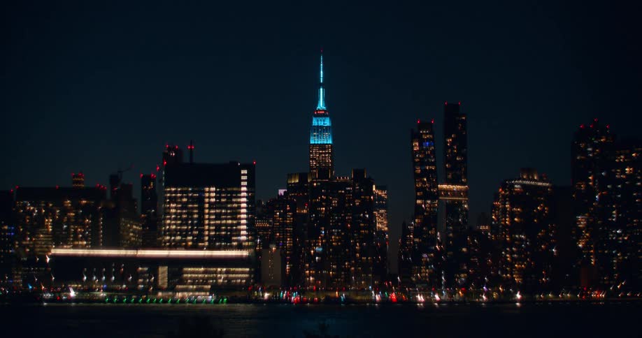 Stunning night shot of the New York City skyline, featuring the blue-lit Empire State Building, which blurs into a beautiful bokeh
