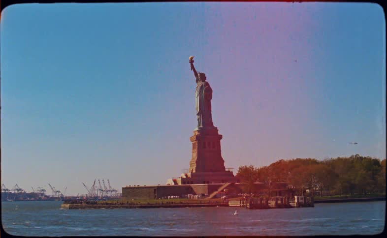 A vintage, grainy film captures a sunlit view of the Statue of Liberty from the water in New York City