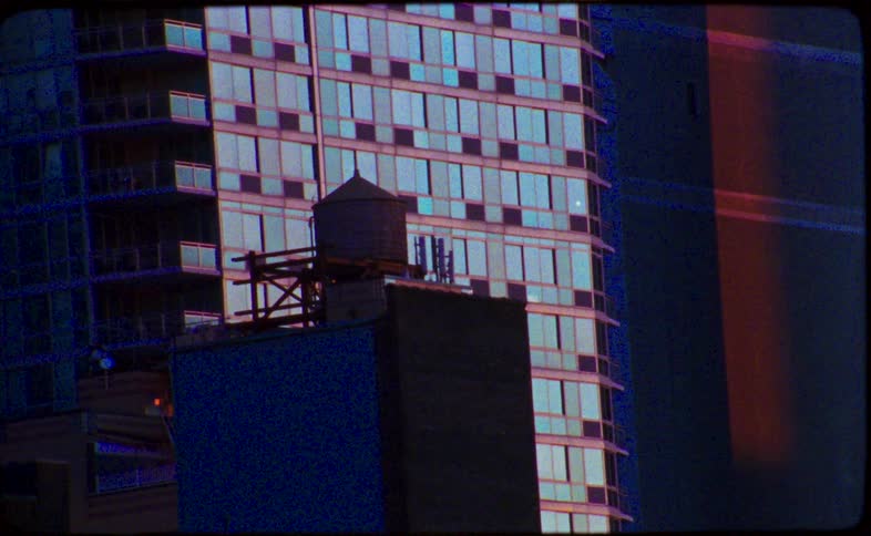 16mm film captures an iconic New York City water tower silhouetted against a modern glass building during a vibrant sunset