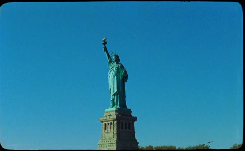 A vintage, archival shot from a moving boat tilts up to reveal the iconic Statue of Liberty against a clear blue sky