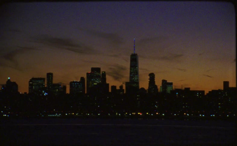 A vintage film pan across the silhouetted industrial waterfront and skyline of New York City at dusk