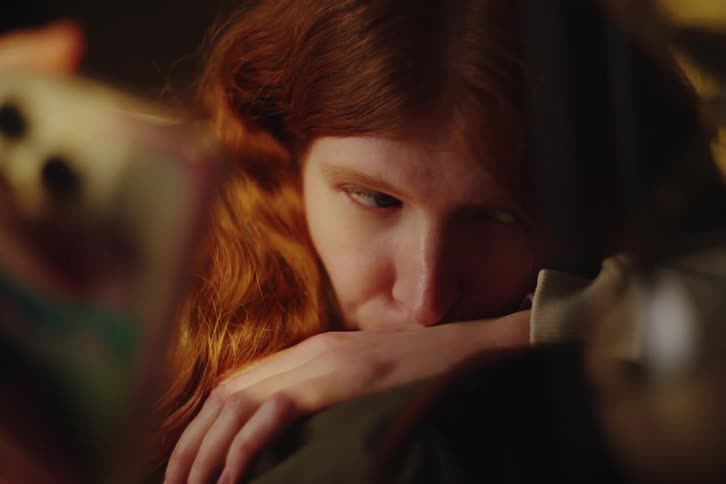 Close-up of a melancholic redhead looking at her phone with a pensive and sad expression in a warm, dark room