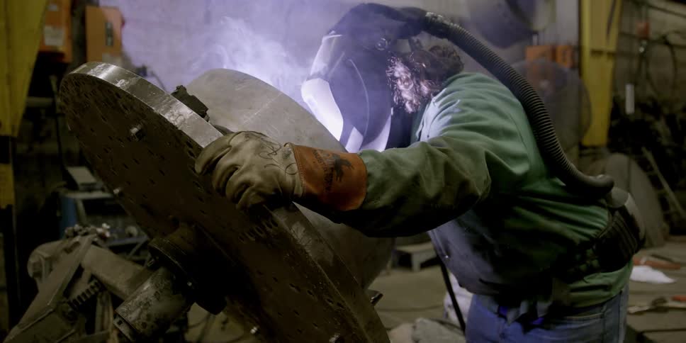 A man is welding a large metal cap
