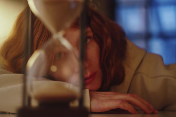 Close up of a pensive redhead woman watching the sand fall through an hourglass as time passes by