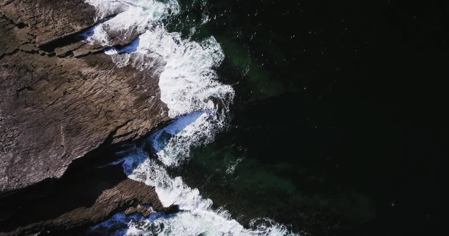 Waves crash against the rocks below causing suds