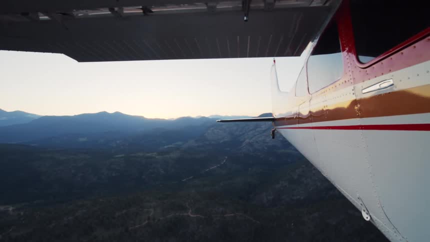 A serene view from a small plane flying over a vast, mountainous forest landscape at sunset