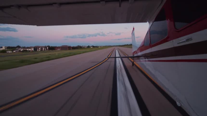 A pov shot from the wing of a small propeller plane as it lands on a rural runway during a beautiful sunset