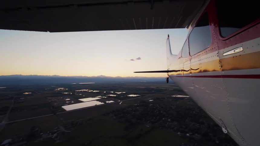 A scenic aerial view from a small plane flying over a rural landscape with distant mountains at sunset