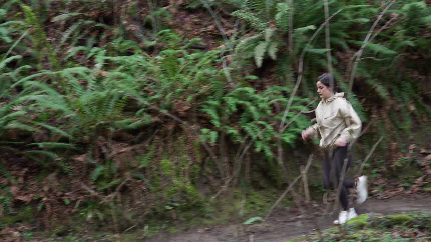Slow-motion side profile of a young woman running along a dirt trail through a lush, green forest