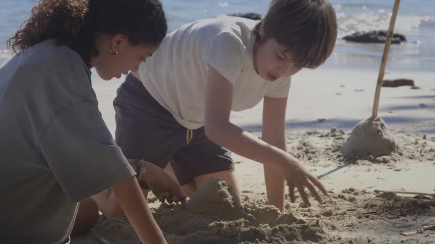 A young boy and girl concentrate as they build a sandcastle together on the beach by the water