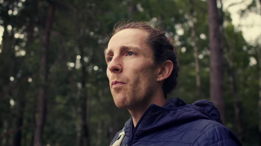 Low-angle slow-motion shot of a male hiker taking a drink from a white water bottle in a lush green forest