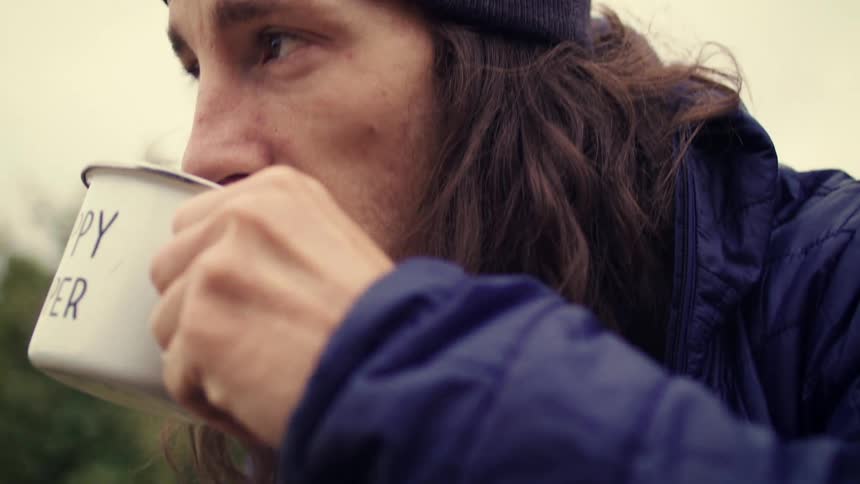 Slow motion close-up of a man in outdoor gear drinking from a white camping mug with the words 'Happy Camper'