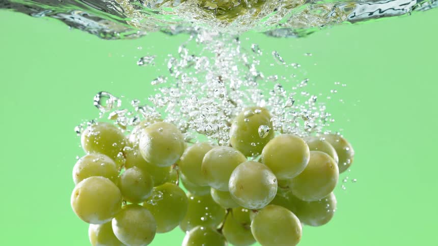 A fresh bunch of green grapes makes a splash as it is submerged in water in super slow motion against a green screen background