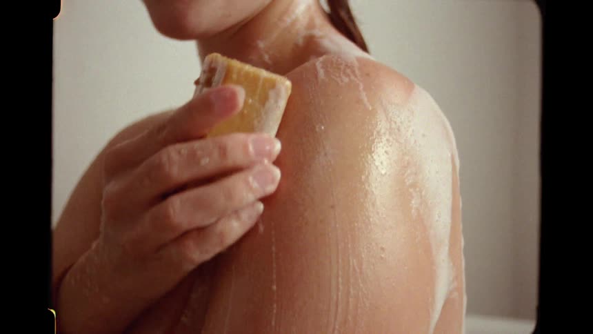 Vintage-style close-up of a woman gently washing her shoulder with a bar of soap in the shower