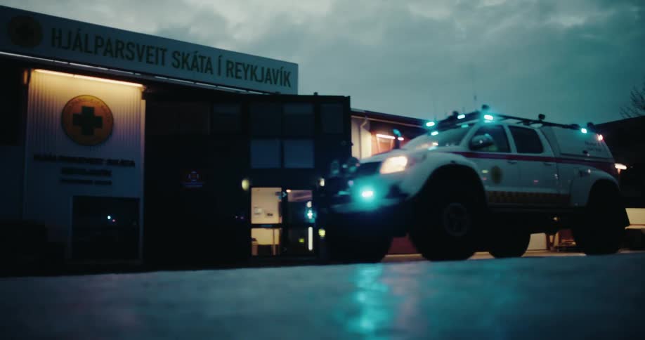 An Icelandic search and rescue vehicle with flashing blue lights departs its station on a cold, snowy night for an urgent mission