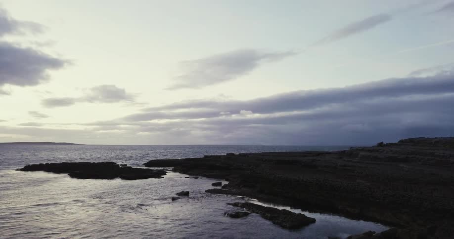 The waves crash against the shoreline at dusk