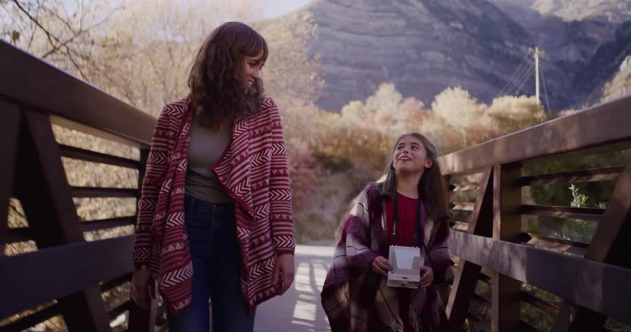 Slow motion shot tilts up as a happy mother and daughter walk together across a wooden bridge in a mountain canyon