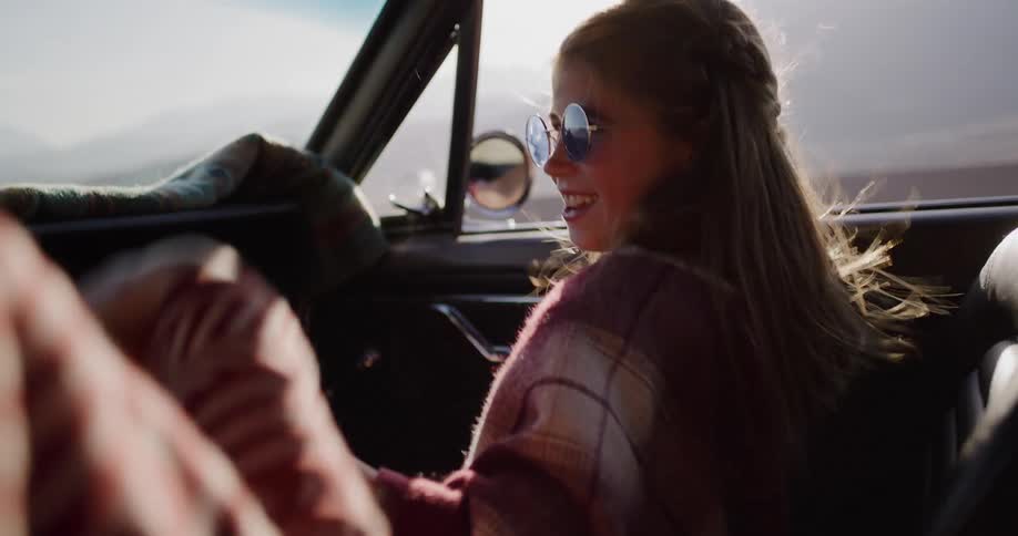 Happy young girl with sunglasses laughs and enjoys the ride in a vintage convertible car on a sunny day road trip