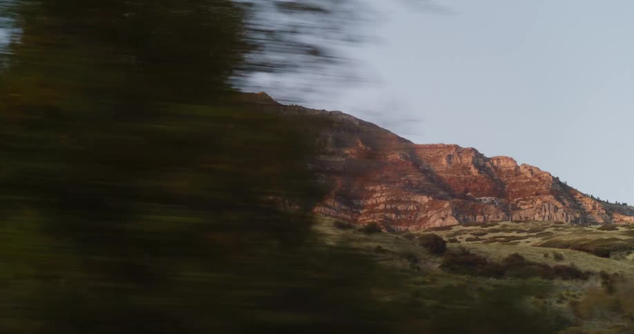 A scenic drive reveals a majestic, rocky mountain range illuminated by the warm light of golden hour