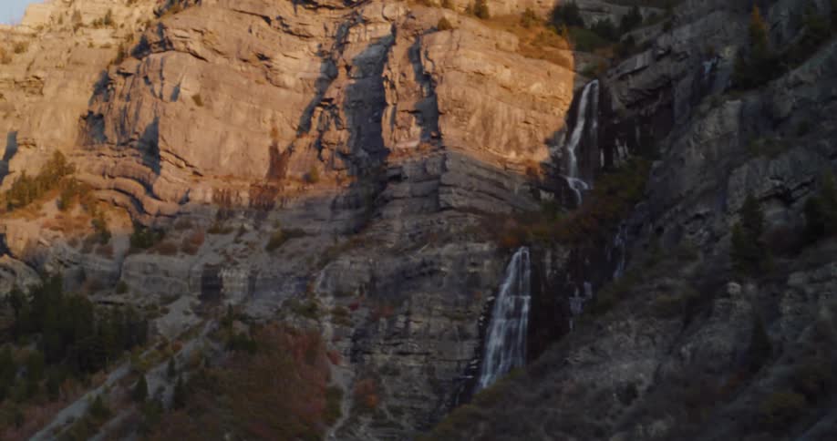 A classic muscle car drives along a scenic highway, revealing a majestic waterfall cascading down a sun-kissed mountain at golden hour