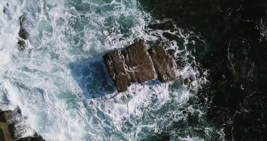 Ocean waves crash into a large boulder