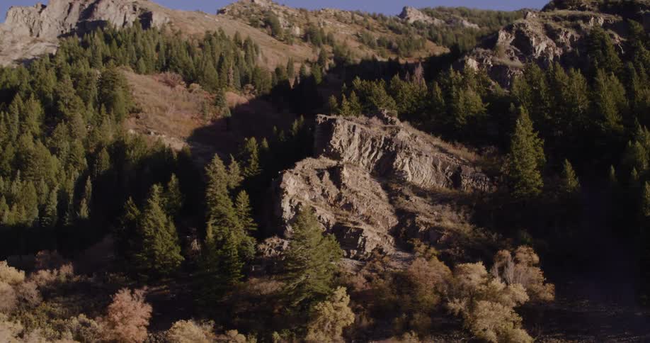 A slow pan reveals a rocky, tree-covered mountain on a sunny day