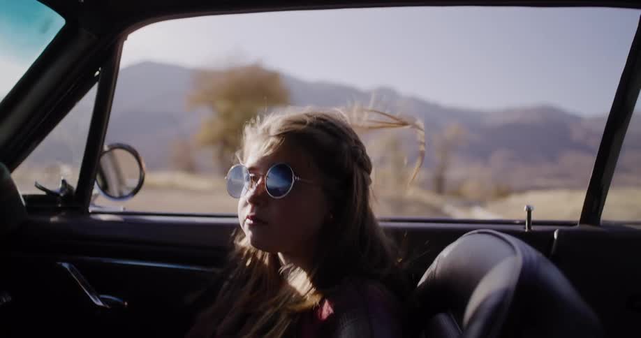 Slow motion shot of a stylish young girl with sunglasses singing in a classic convertible car on a sunny road trip