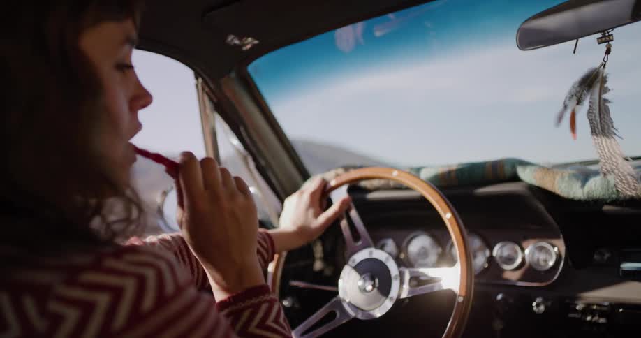 A young woman enjoys a piece of red licorice while driving a classic car on a sunny day road trip