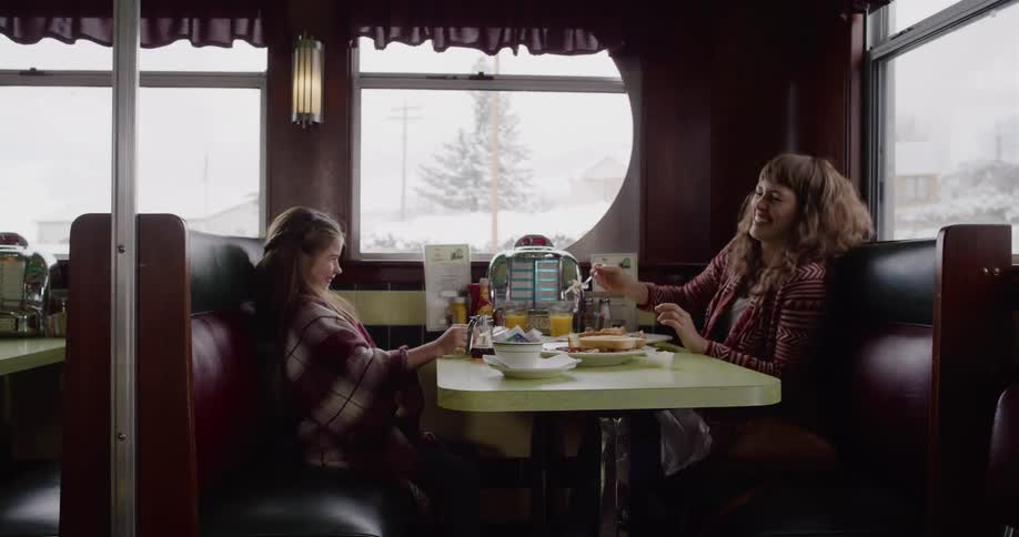 A mother and daughter share a warm meal together inside a cozy diner on a snowy day
