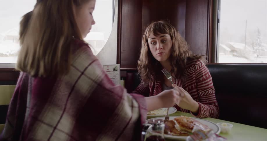 A mother and daughter enjoy a slow-motion breakfast together in a cozy diner on a snowy day