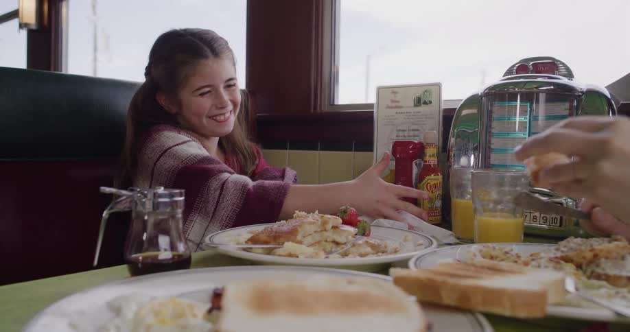 A happy young girl enjoys pancakes for breakfast with her mother in a classic diner