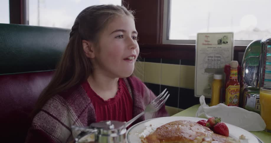 Happy young girl takes a big bite of pancakes and gives a thumbs up in a diner booth in slow motion