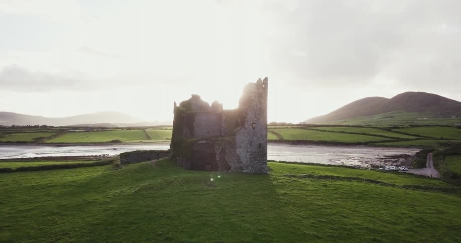 A broken tower sits near the water on a hill