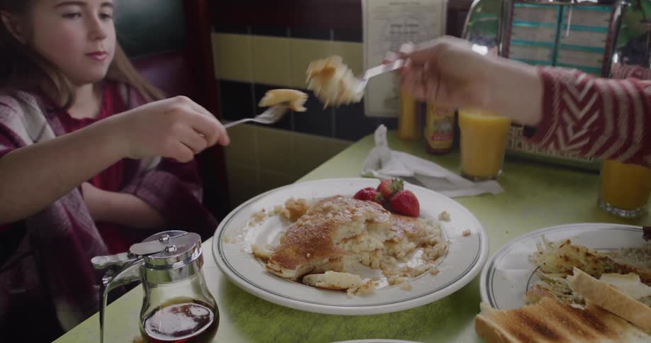 Slow motion shot of a mother and daughter sharing and eating a delicious pancake breakfast at a classic diner