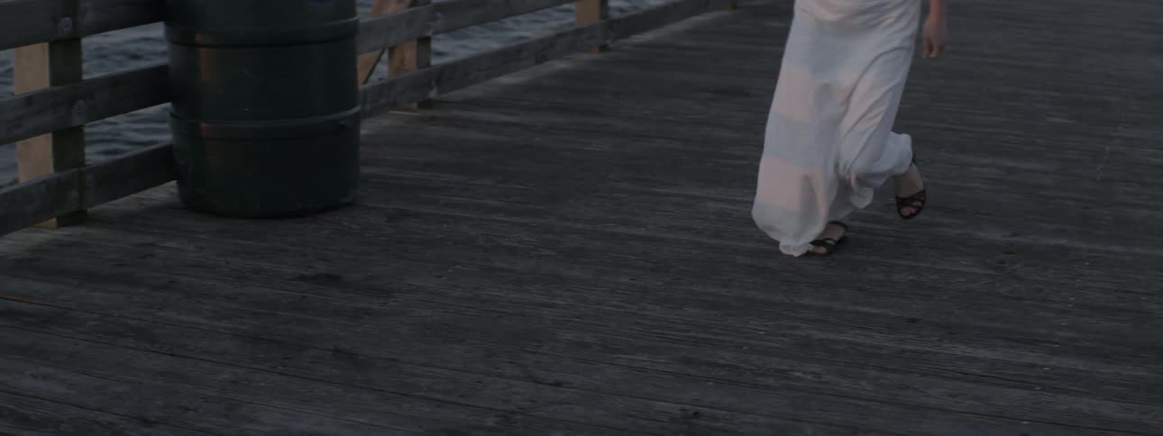 Woman wearing long white dress starts running on a wooden boardwalk