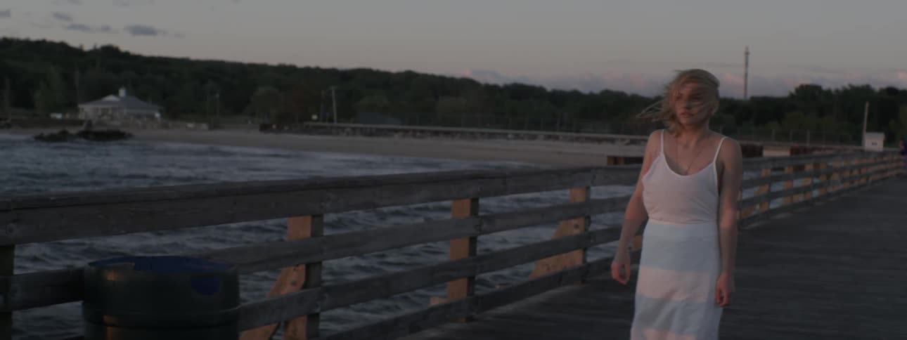 A woman stands on an ocean pier on a windy day