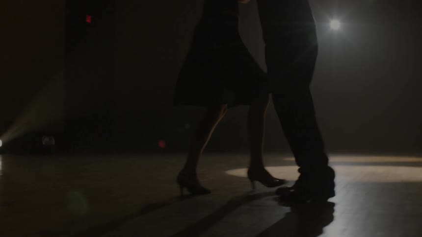 Two people are dancing on a dark stage