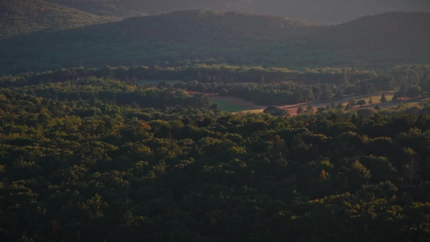 A majestic aerial shot ascends over a sprawling green forest at sunrise, revealing a beautiful home and a wide river in the distance