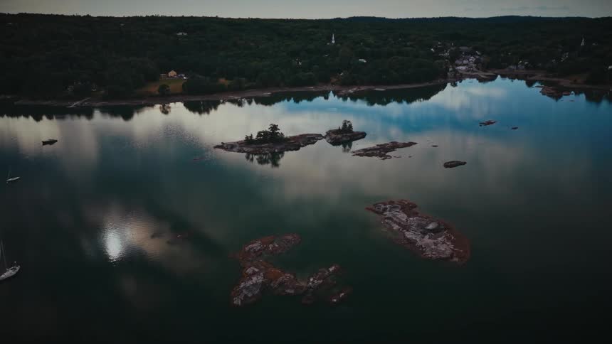 Serene aerial cinemagraph of a forested harbor with rocky islands and glassy, reflective water