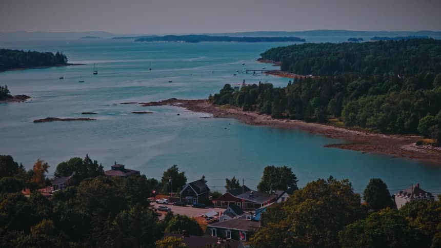 A serene aerial view slowly zooms into a picturesque coastal town nestled along a tranquil blue bay surrounded by forested islands