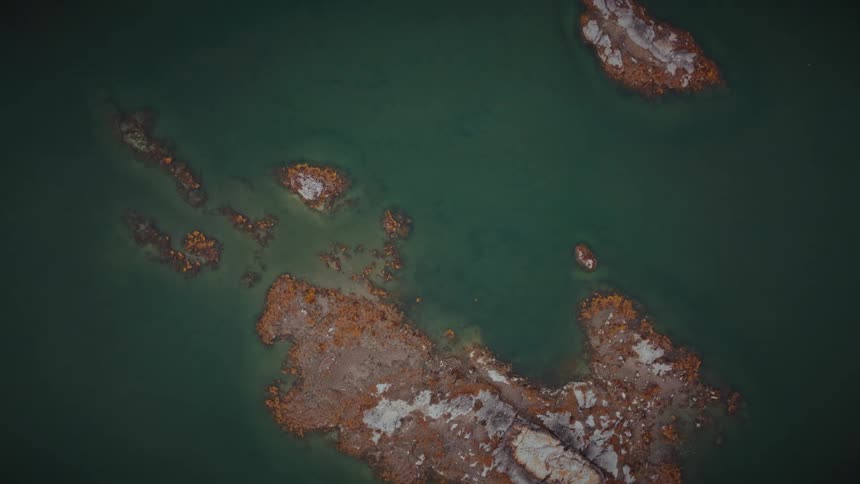 Top-down aerial footage slowly zooms out to reveal rocky, barren islands in a vast, calm, green lake