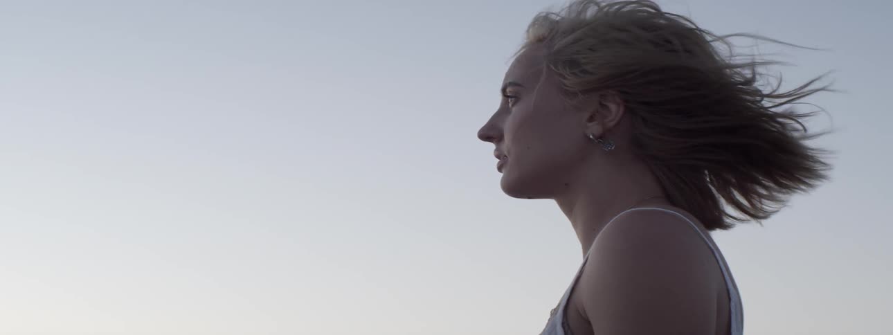 The wind blows a woman's hair around her face as she stands outside
