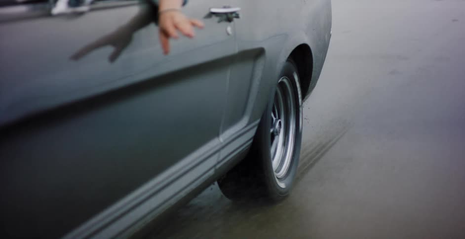 Seamless loop showing a close-up of a vintage muscle car's spinning tire as it drives along a wet, sandy beach