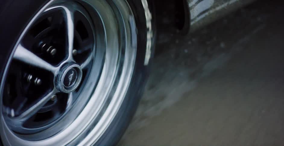 Extreme close-up of a classic Ford Mustang wheel spinning and kicking up water on a wet road