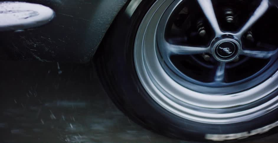 Close-up of a classic Ford Mustang wheel spinning fast on a wet road, kicking up water