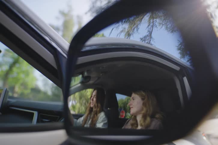 Close-up of a car's side-view mirror showing the reflection of two friends talking and smiling
