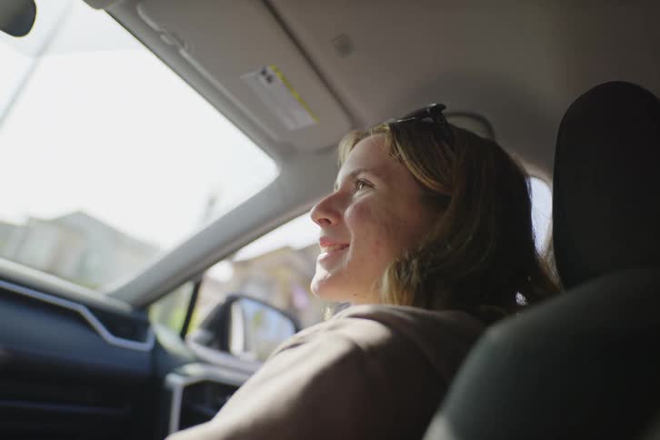 Sunlight warms the face of a happy young woman as she enjoys a car ride from the passenger seat